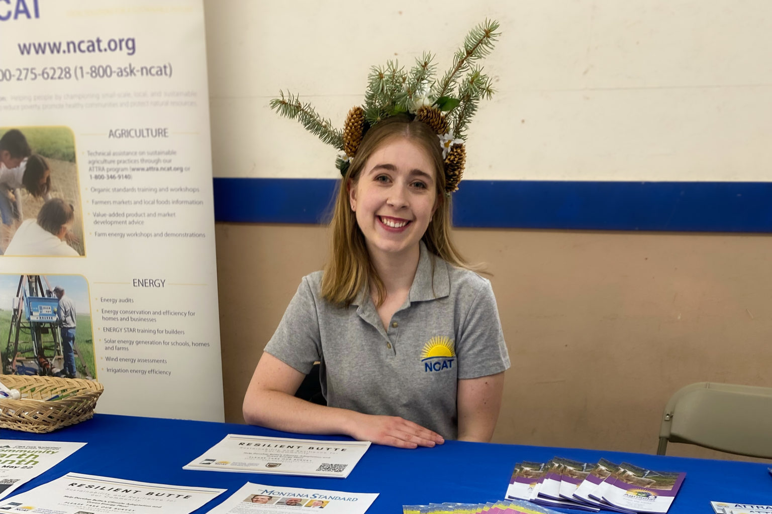 a smiling woman sitting at a table wearing a NCAT t-shirt