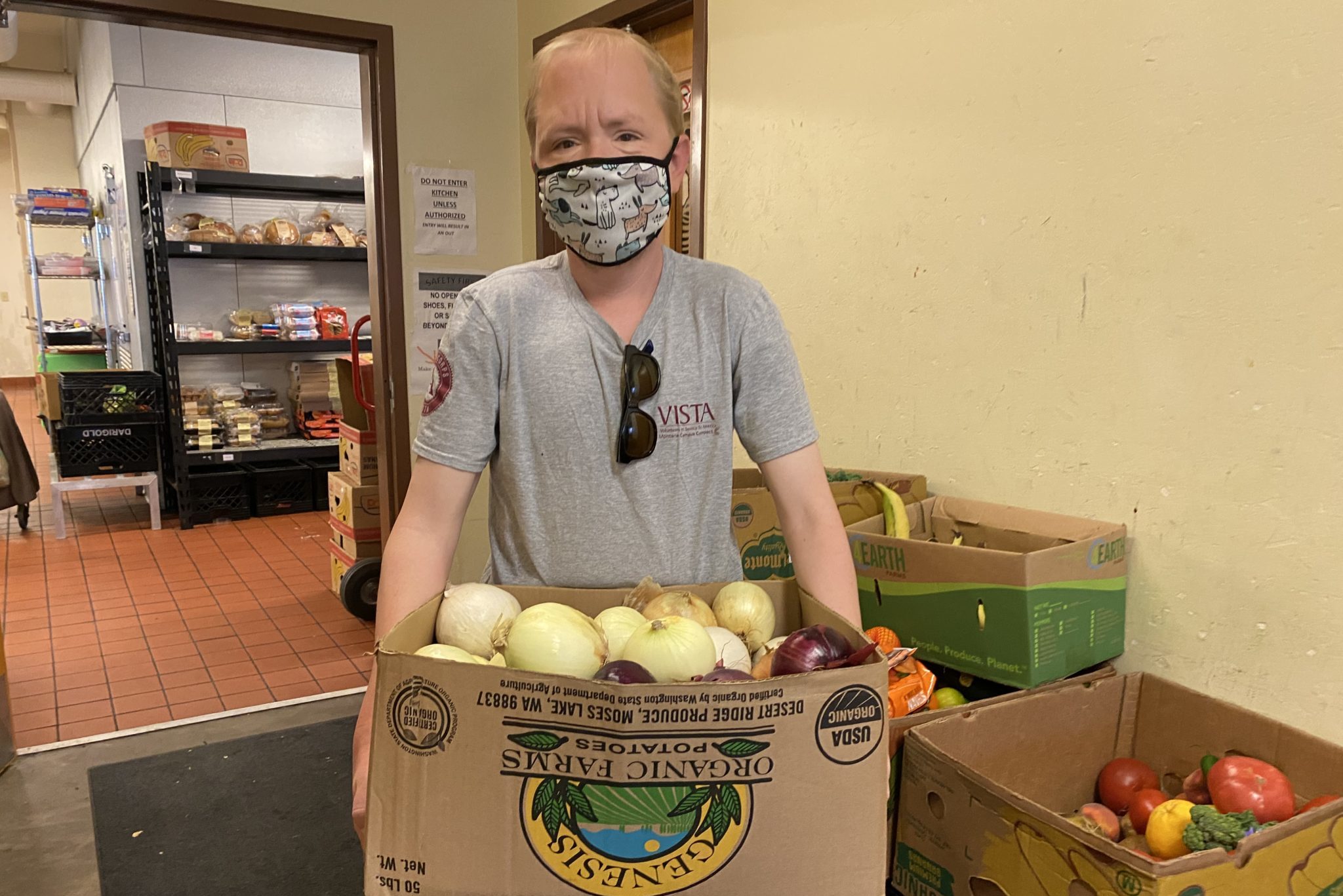 a person holding a box of onions and wearing a VISTA shirt