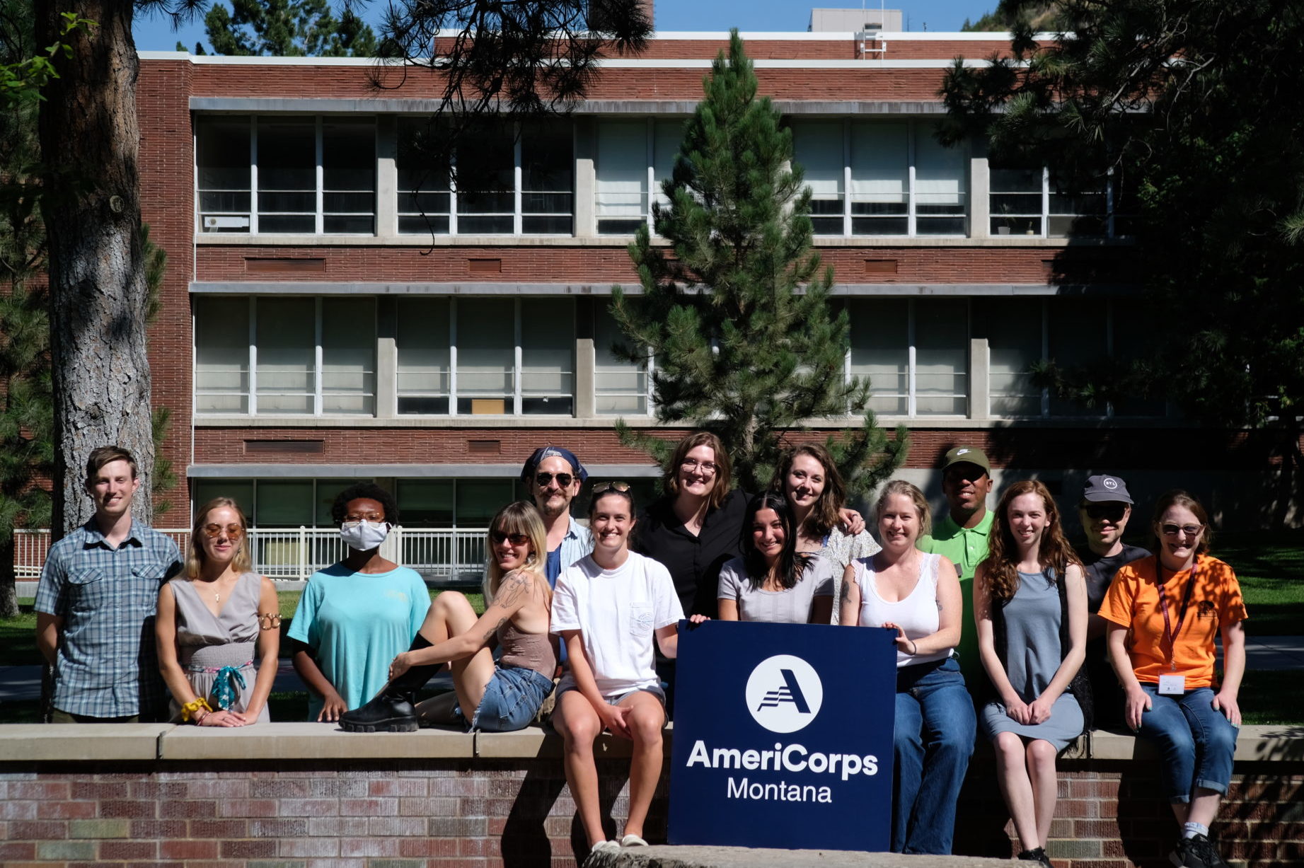 a group of people sitting on a long brick bench smiling and holding an AmeriCorps sign