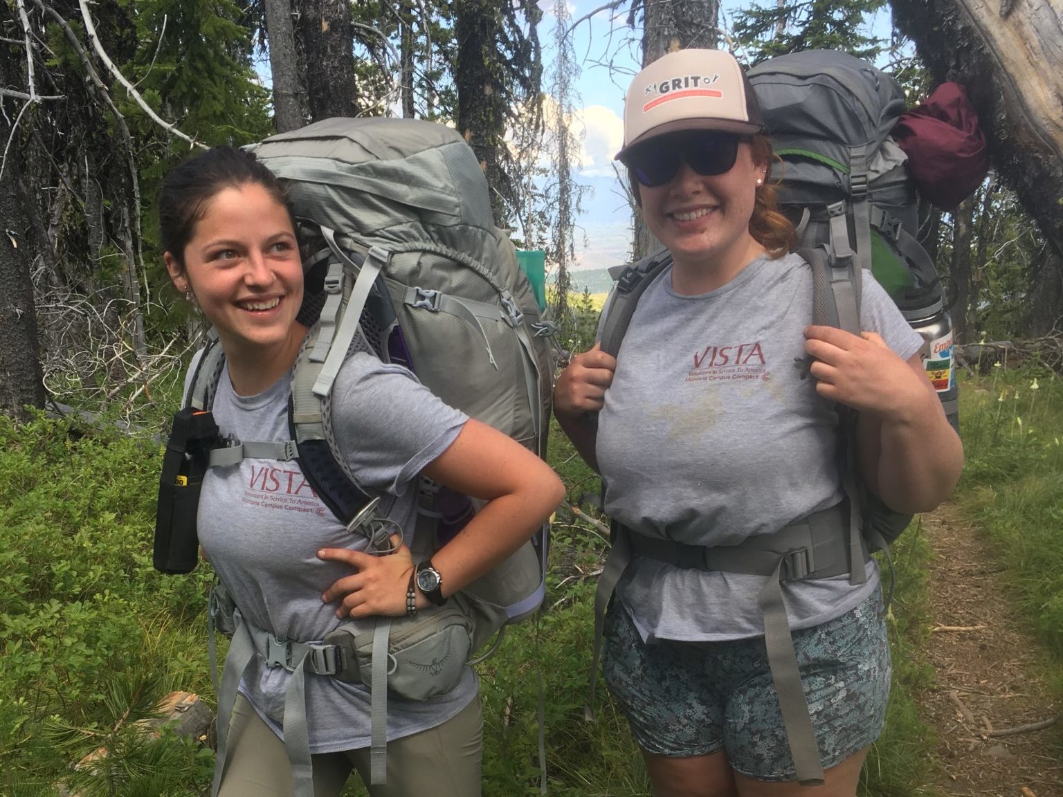 Two AmeriCorps members wearing backpacking gear in the woods.