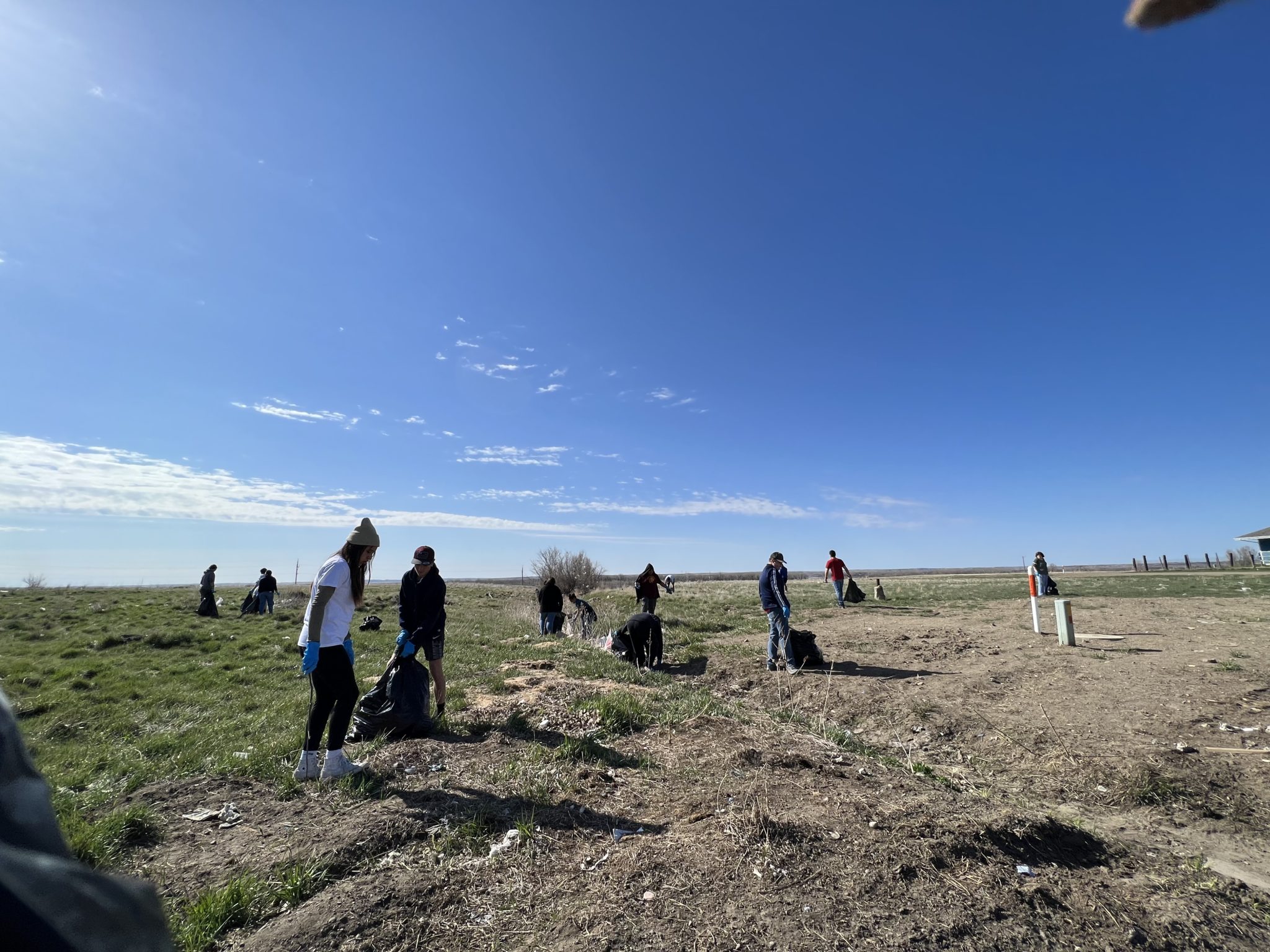 Nine individuals walking around an open field. They are placing trash into large black bags.