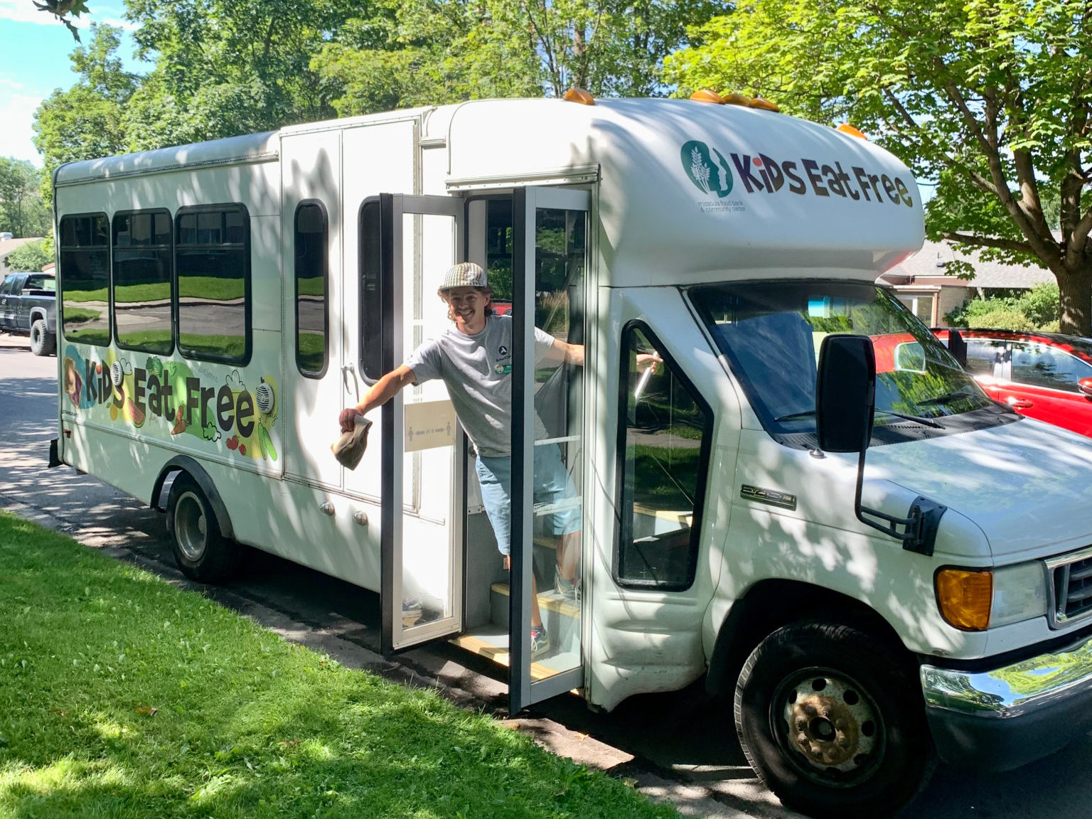 An AmeriCorps member standing in the door of a white bus. The bus has the "Kids eat free" written on the side.